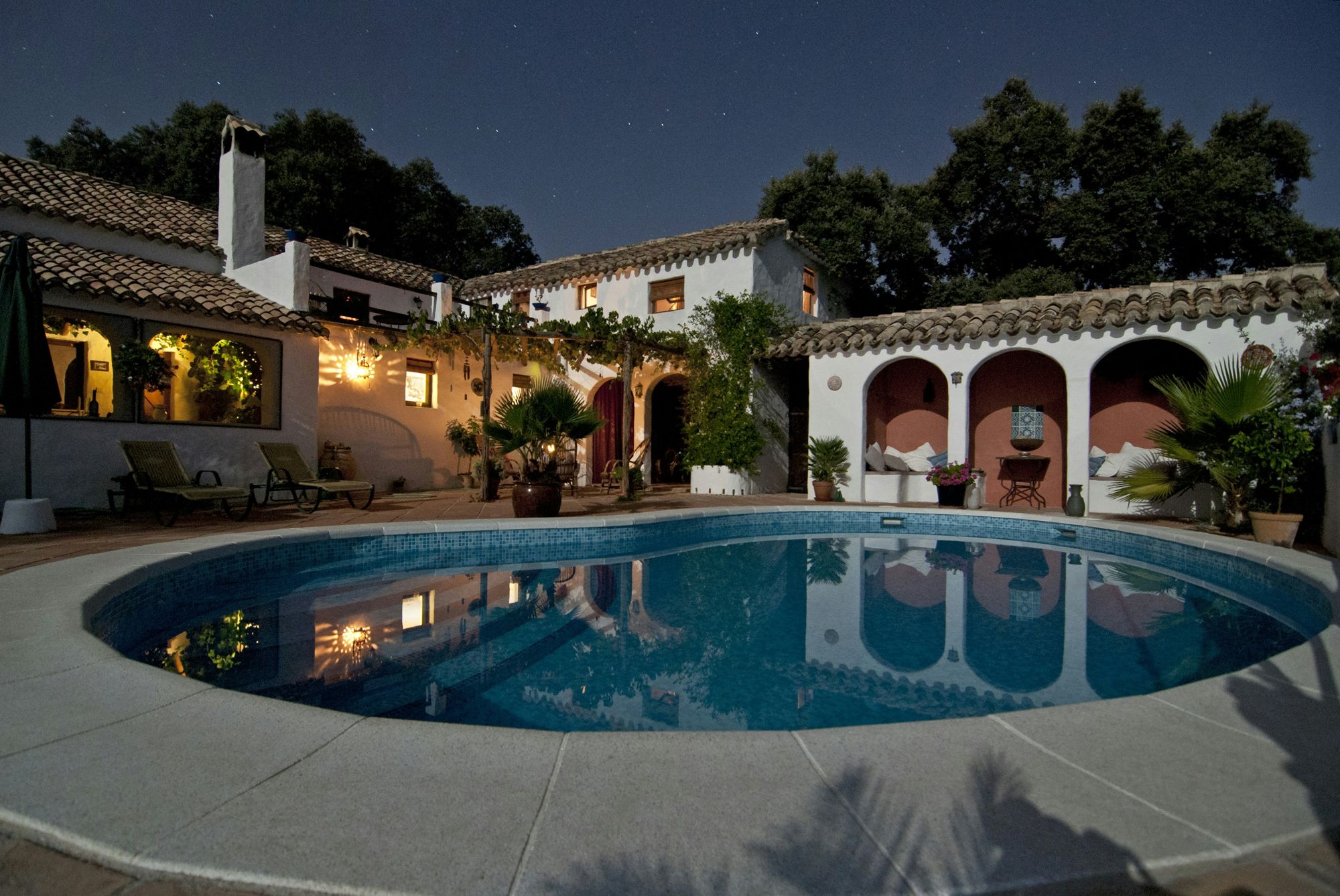 Rambling ranch estate at night with a resort-style pool, arched cabana and glowing terraces
